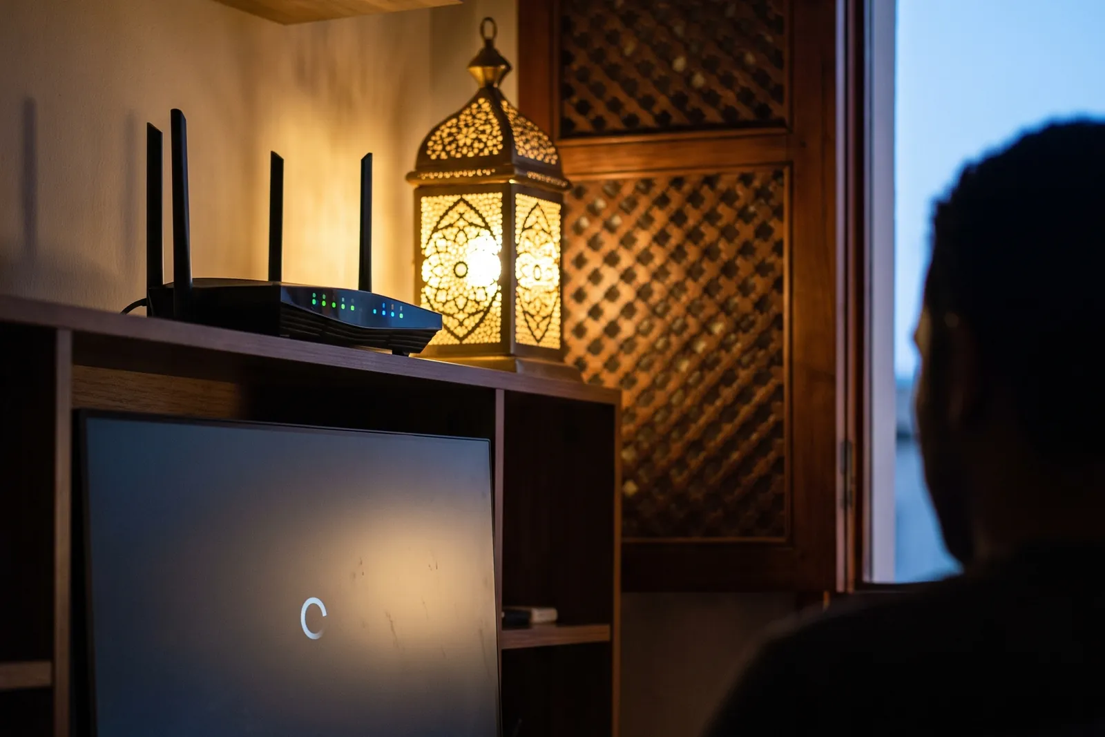 Écran bloqué sur une icône de chargement et routeur Wi-Fi posé sur une étagère, dans une maison marocaine le soir