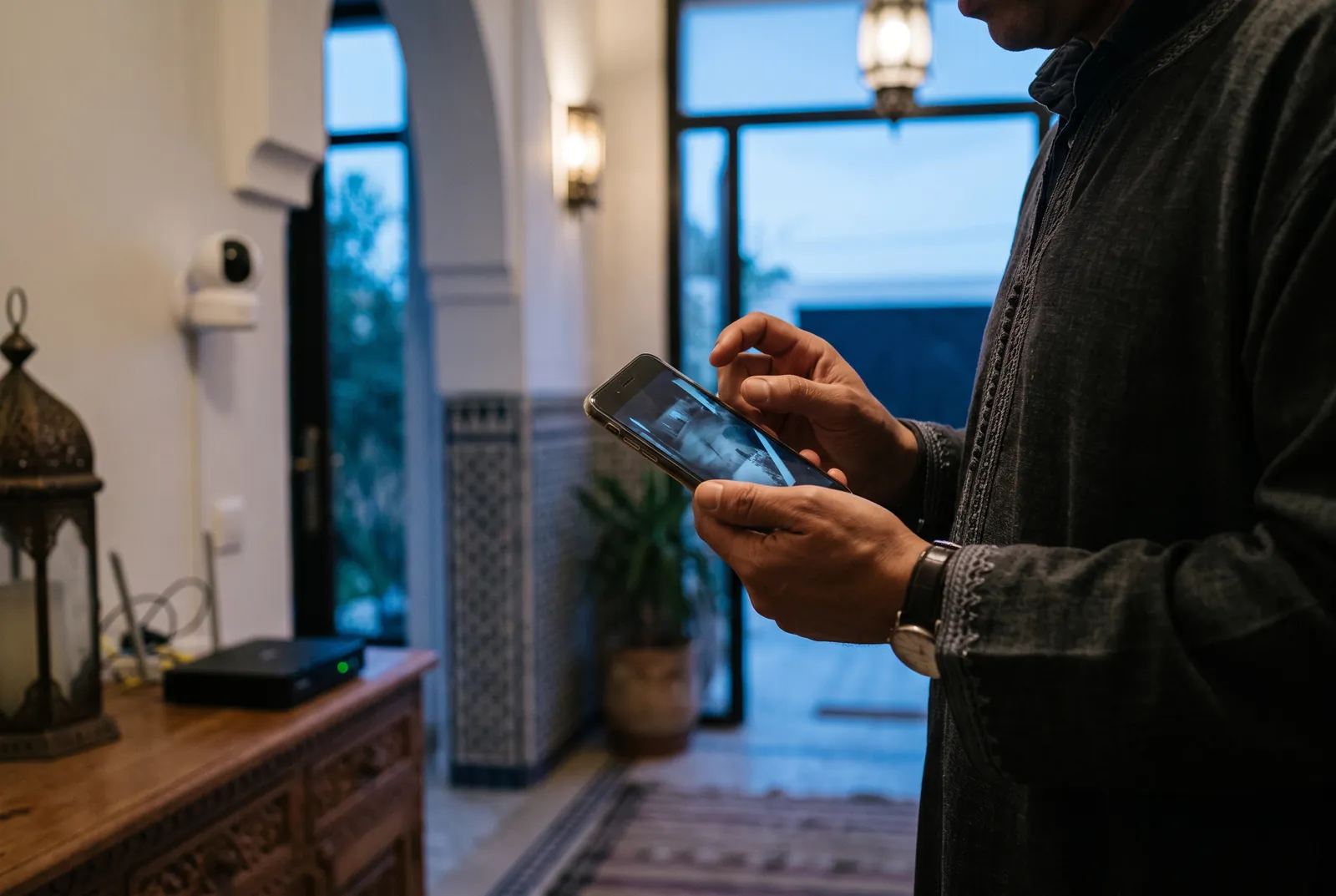 Propriétaire consultant sur son smartphone l'image d'une caméra de surveillance Wi-Fi, dans l'entrée d'une villa marocaine