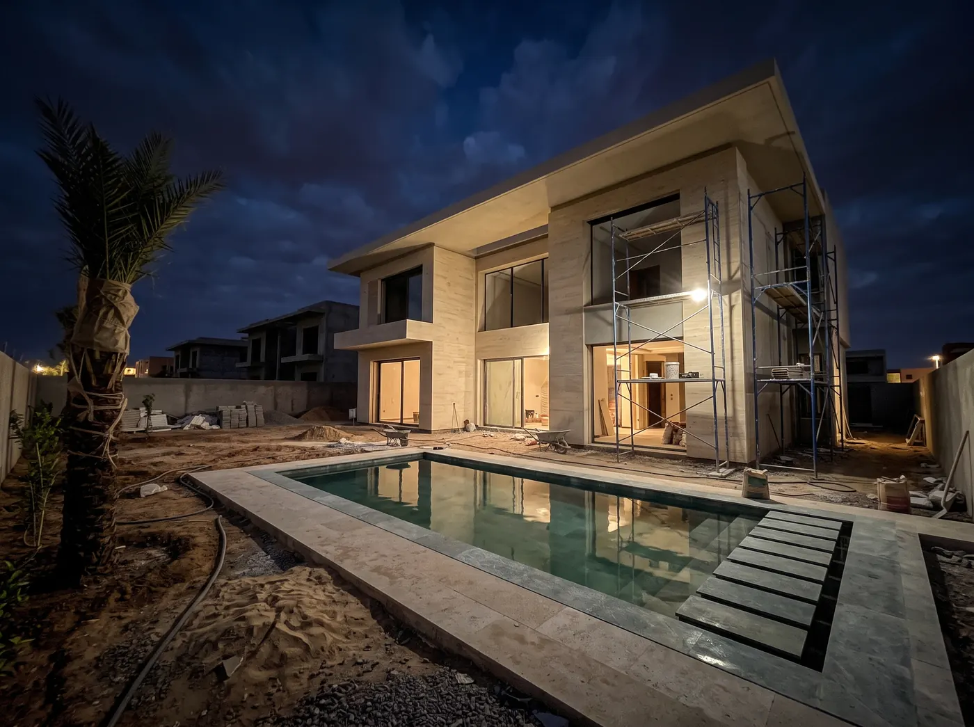 Villa en fin de chantier à la Résidence Noria Golf de Marrakech, éclairée à la tombée de la nuit : façade en pierre, échafaudages et piscine