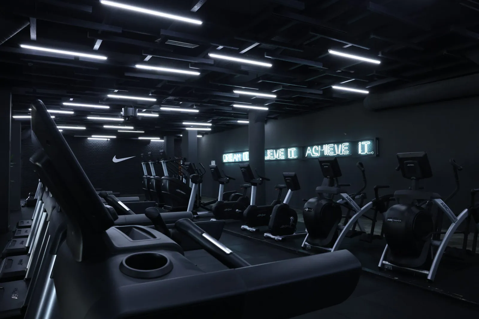 Salle de sport moderne avec appareils de cardio et éclairage linéaire au plafond